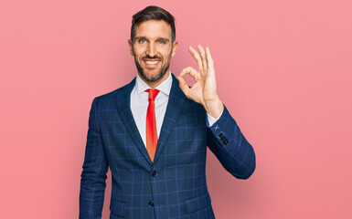 Handsome man with beard wearing business suit and tie smiling positive doing ok sign with hand and fingers. successful expression.