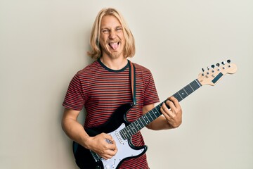Fototapeta premium Caucasian young man with long hair playing electric guitar sticking tongue out happy with funny expression.