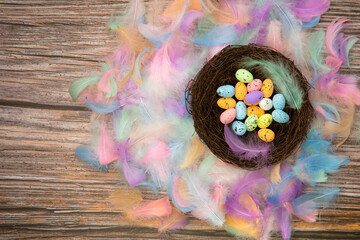 Colorful bright easter eggs in bird nest with Pastel colored feathers and wooden background texture top view, Copy Space, Spring, Easter Holliday, greeting card concept