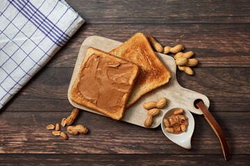 Sweet breakfast with peanut butter toast and peanuts on a wooden cutting board