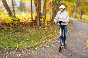 Grauhaarige Weißhaarige Frau fährt E Scooter in Park in Helm