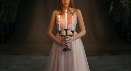 Art photo. medieval girl princess standing in dark gothic room. Woman queen is holding candlestick...