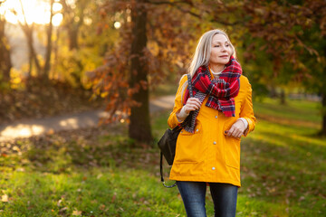 Weißhaarige Grauhaarige Frau spaziert im Park Herbst Sonnenstrahlen gelbe Regenmantel 