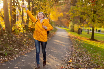 Weißhaarige Grauhaarige Frau spaziert im Park Herbst Sonnenstrahlen gelbe Regenmantel 