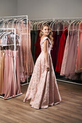 Young beautiful blonde girl wearing a full-length draped one shoulder pale pink satin slit prom...