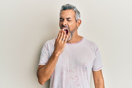 Middle age grey-haired man wearing casual clothes bored yawning tired covering mouth with hand. restless and sleepiness.