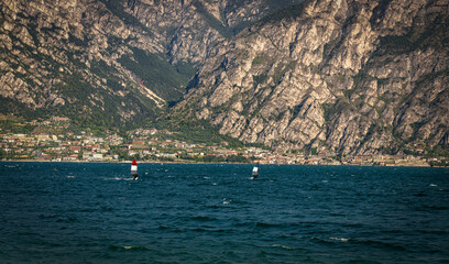 Fototapeta na wymiar Windsurfing on the gardasee surface with mountains in the background.