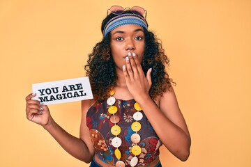 Young african american woman wearing bohemian and hippie style holding you are magical message covering mouth with hand, shocked and afraid for mistake. surprised expression