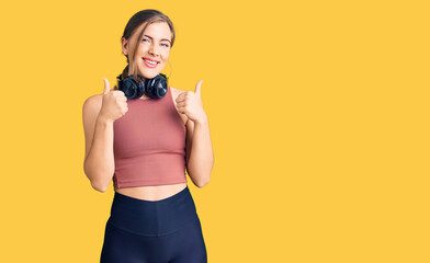 Beautiful caucasian young woman wearing gym clothes and using headphones success sign doing positive gesture with hand, thumbs up smiling and happy. cheerful expression and winner gesture.