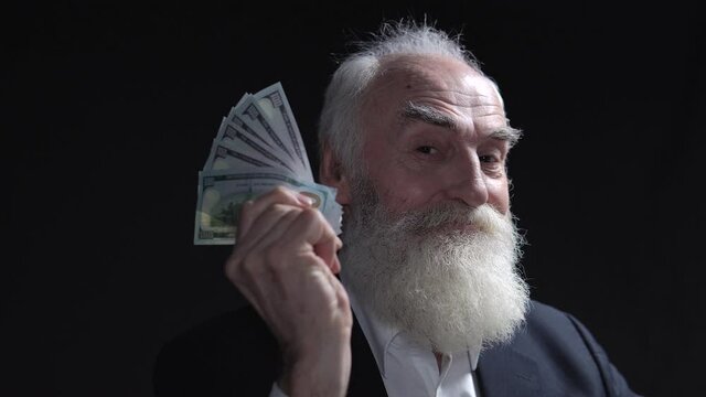 Successful rich man with gray beard bragging holding fan of dollars in his hand