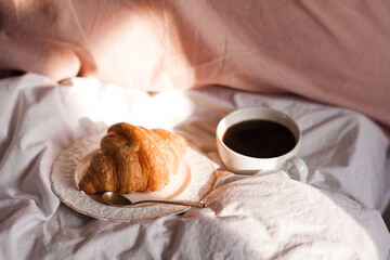 Cup of fresh coffee with croissant on white plate in bed closeup. Breakfast time. Good morning.