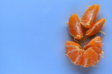 One fresh peeled tangerine with three slices on a blue-colored table view from above with a copy space. High quality photo