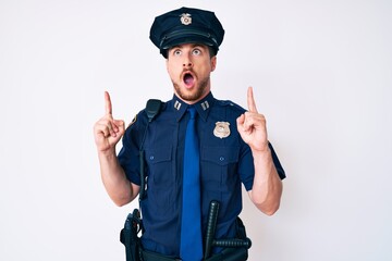 Young caucasian man wearing police uniform amazed and surprised looking up and pointing with fingers and raised arms.