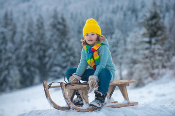 Winter kids. Child boy sliding on a sled in snowy park. Little boy playing outdoors in the snow.