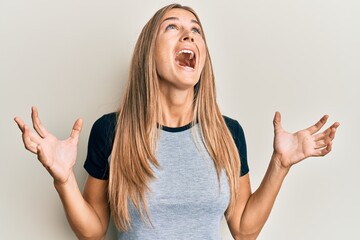 Young blonde woman wearing casual clothes crazy and mad shouting and yelling with aggressive expression and arms raised. frustration concept.