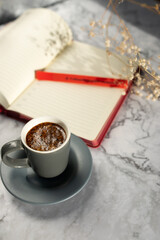 
a cup of coffee on the table with a notebook and a pen