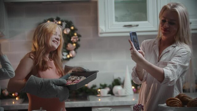 Happy family christmas - daughter takes out the baking sheet and her proud mom taking pictures of her