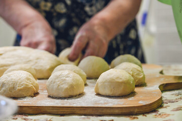 Baker makes dough and rolls dough balls on wooden board. Preparation for cooking pastries.