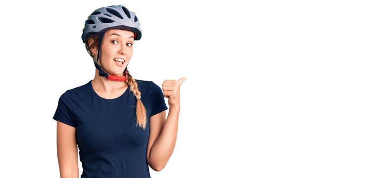Beautiful caucasian woman wearing bike helmet smiling with happy face looking and pointing to the side with thumb up.