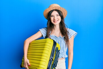 Young beautiful caucasian girl wearing summer dress and holding cabin bag looking positive and happy standing and smiling with a confident smile showing teeth