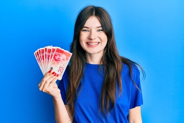 Young beautiful caucasian girl holding 20 israel shekels banknotes looking positive and happy...