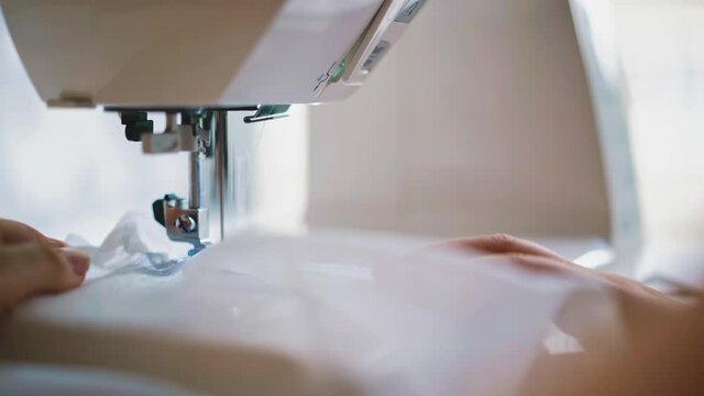 close up: hands of young woman sews on an automatic sewing machine transparent fabric, tulle, toss, is at home on self-isolation, quarantine, during pandemic