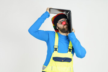 A clown in bright clothes holds a laptop above his head.