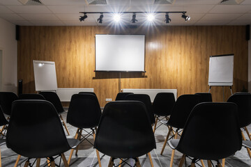 Interior of empty conference hall with black chairs, flipcharts and white screen. 