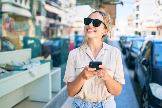 Young beautiful blonde caucasian woman smiling happy outdoors on a sunny day using smartphone
