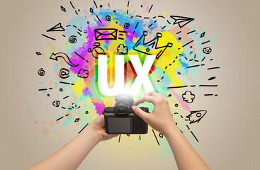 Close-up of a hand holding digital camera with abstract drawing and UX inscription