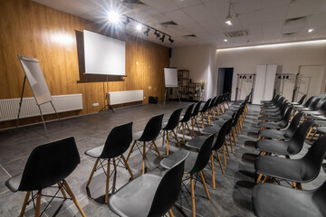 Interior of empty conference hall with black chairs, flipcharts and white screen. 