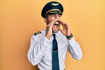 Handsome hispanic man wearing airplane pilot uniform shouting angry out loud with hands over mouth © Krakenimages.com
