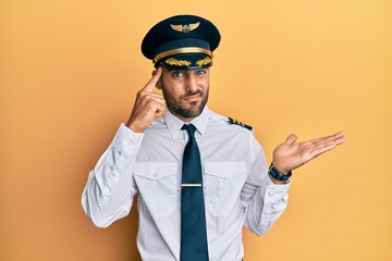 Handsome hispanic man wearing airplane pilot uniform confused and annoyed with open palm showing copy space and pointing finger to forehead. think about it. © Krakenimages.com