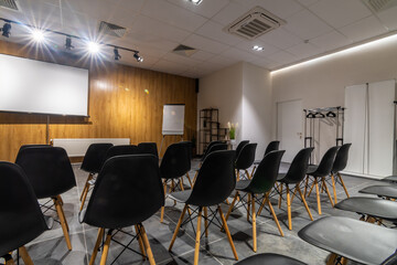 Interior of empty conference hall with black chairs, flipcharts and white screen. 