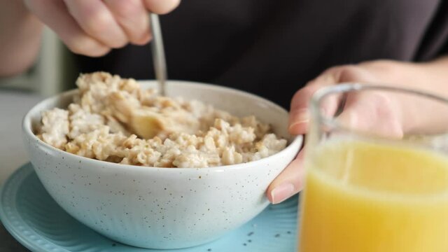 Unrecognizable woman eating oatmeal porridge with bananas and glass of orange juice for breakfast