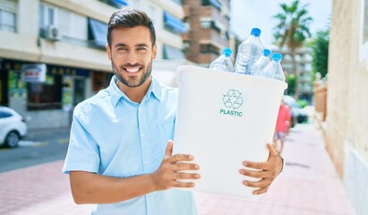 Young hispanic man smiling happy recycling. Holding full bin of plastic bottle at street of city. © Krakenimages.com