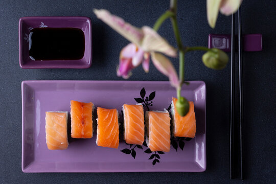 Sushi on a plate, soy sauce, sticks, archidea flower. Dark photo. Flat lay.