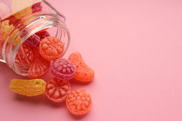 Obraz na płótnie Canvas Sweet fruit hard candies pouring out of the glass mason jar on colored pink background. Overhead view of colorful caramel assortment.