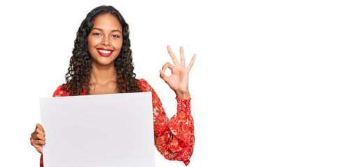 Young african american girl holding blank empty banner doing ok sign with fingers, smiling friendly gesturing excellent symbol