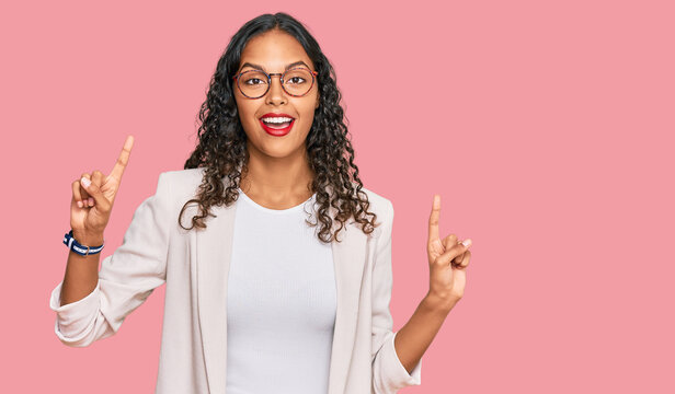Young african american girl wearing business clothes smiling amazed and surprised and pointing up with fingers and raised arms.