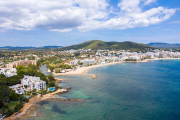 Fototapeta na wymiar Aerial drone photo of the beautiful island of Ibiza in Spain showing the costal front golden sandy beaches with people relaxing and sunbathing on a hot sunny summers day