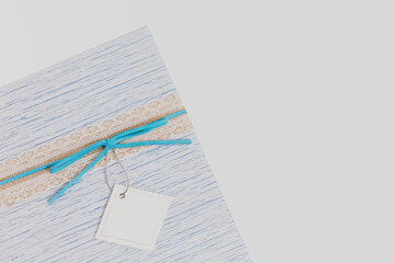 Fragment of gift present box with blue suede bow and blank white paper card at isolated background, backdrop low key, pastel colors