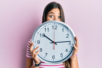 Young brunette woman holding big clock covering face celebrating crazy and amazed for success with...