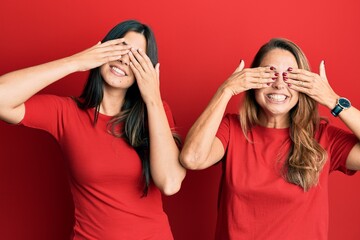 Hispanic family of mother and daughter wearing casual clothes over red background covering eyes with hands smiling cheerful and funny. blind concept.