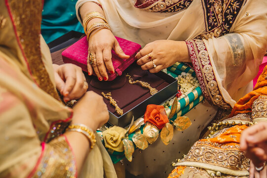 Senior women hands open velvet boxes with golden jewelry earrings for indian bride during wedding henna mehndi sangeet party night 