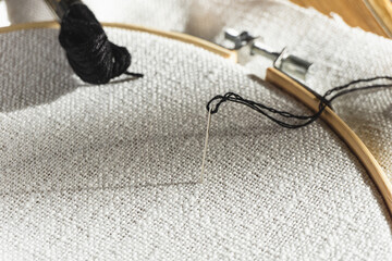 Needle and thread on white fabric inside embroidery hoop