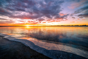 Colorful sunrise over a frozen lake with cracked ice in the foreground