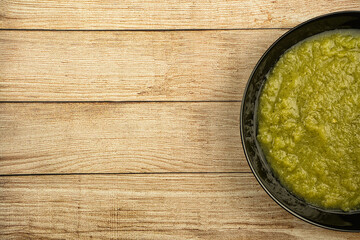 a black plate of fresh vegetable green cream soup served on rustic background