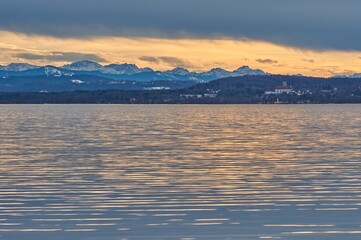 Reflecting lake during sunset with a mountain range in the background. Ammersee lake in Bavaria, Germany during sunset.