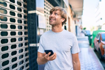 Handsome caucasian man smiling happy outdoors using smartphone